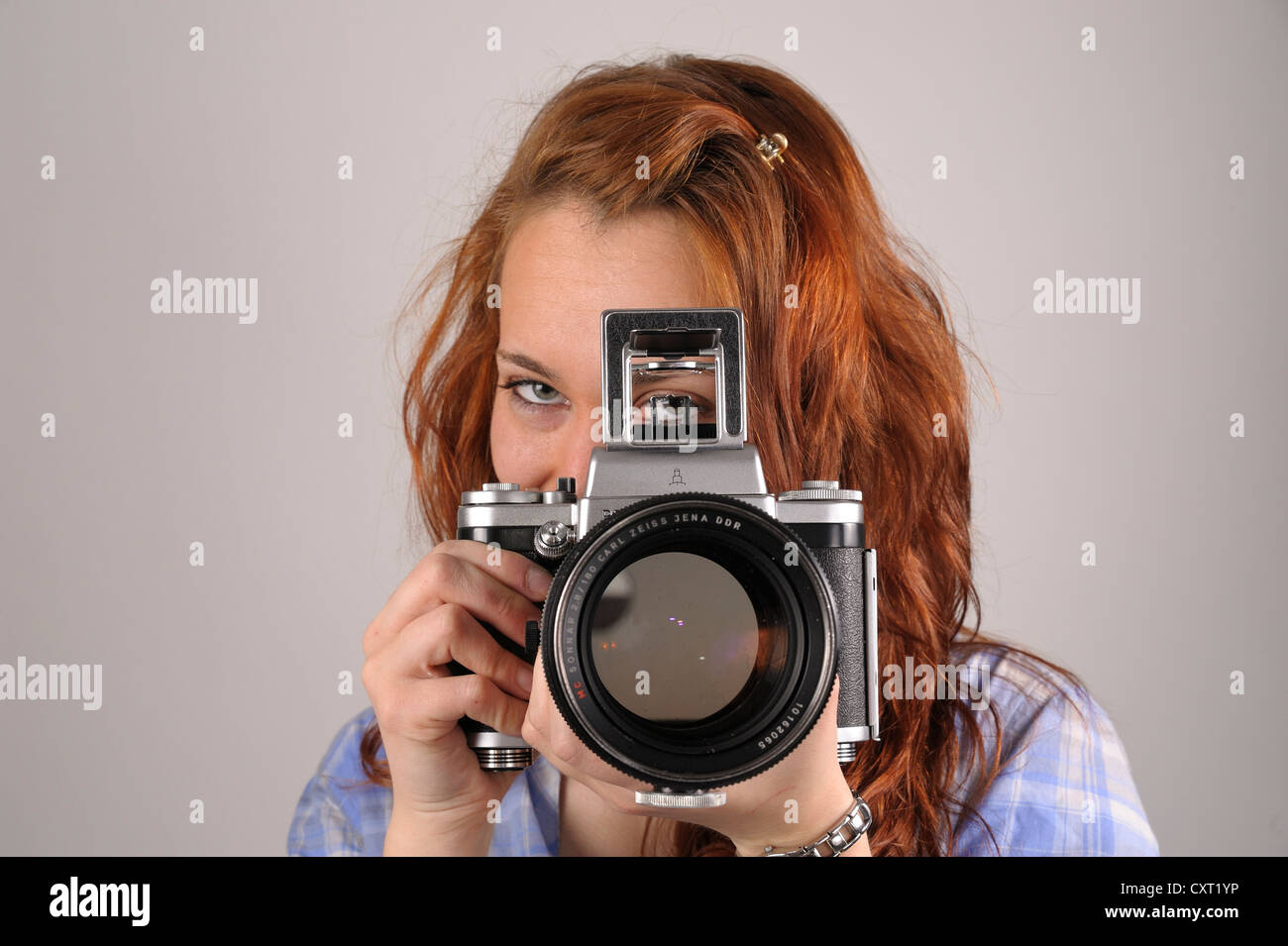 Young woman with red hair taking a photograph with an analog medium format camera Pentacon Six Stock Photo
