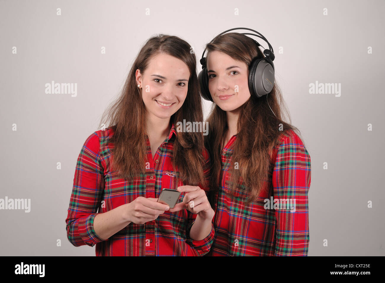 Twin sisters, one holding an iPod, the other listening to headphones Stock Photo