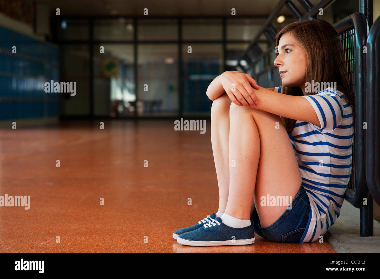 Schoolgirl sitting alone in the school building, leaning against a railing Stock Photo