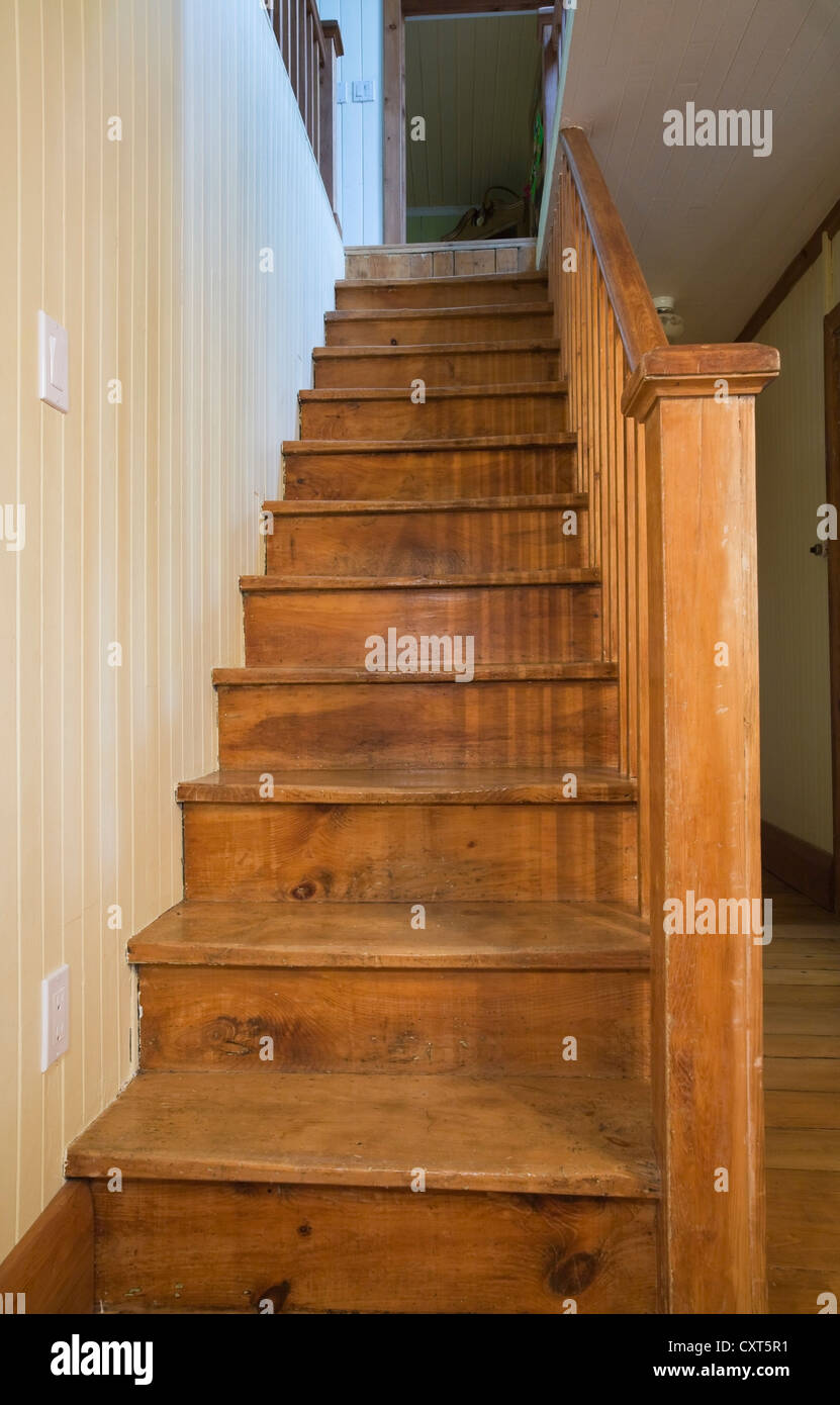 Wooden staircase in the dining room leading to the upstairs floor in an old Canadiana cottage-style residential fieldstone home, Stock Photo