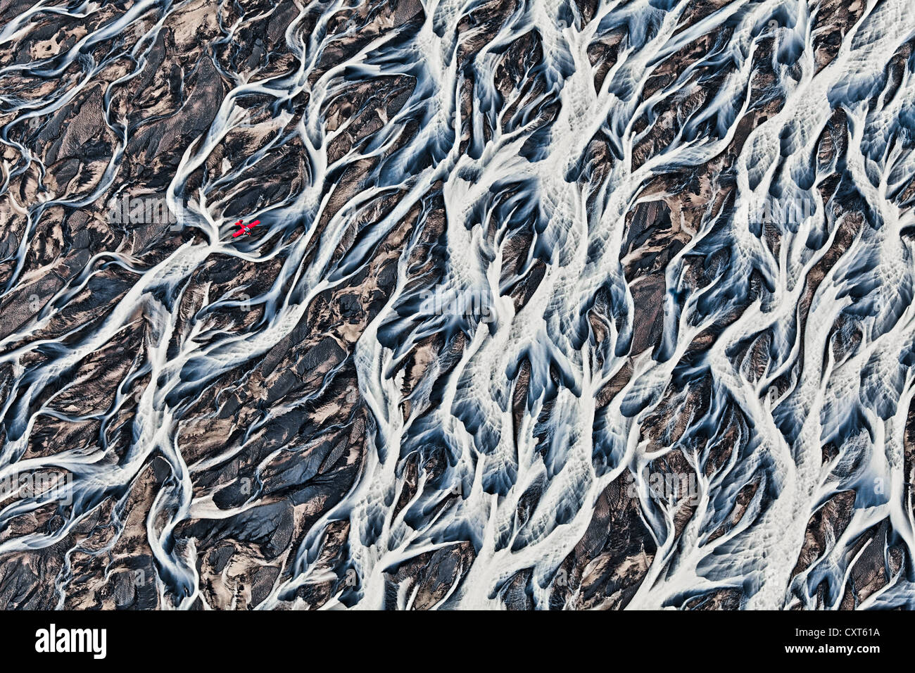 Aerial view, a red single-engine lightweight airplane flying over the flow structures of the melt water branching out in all Stock Photo