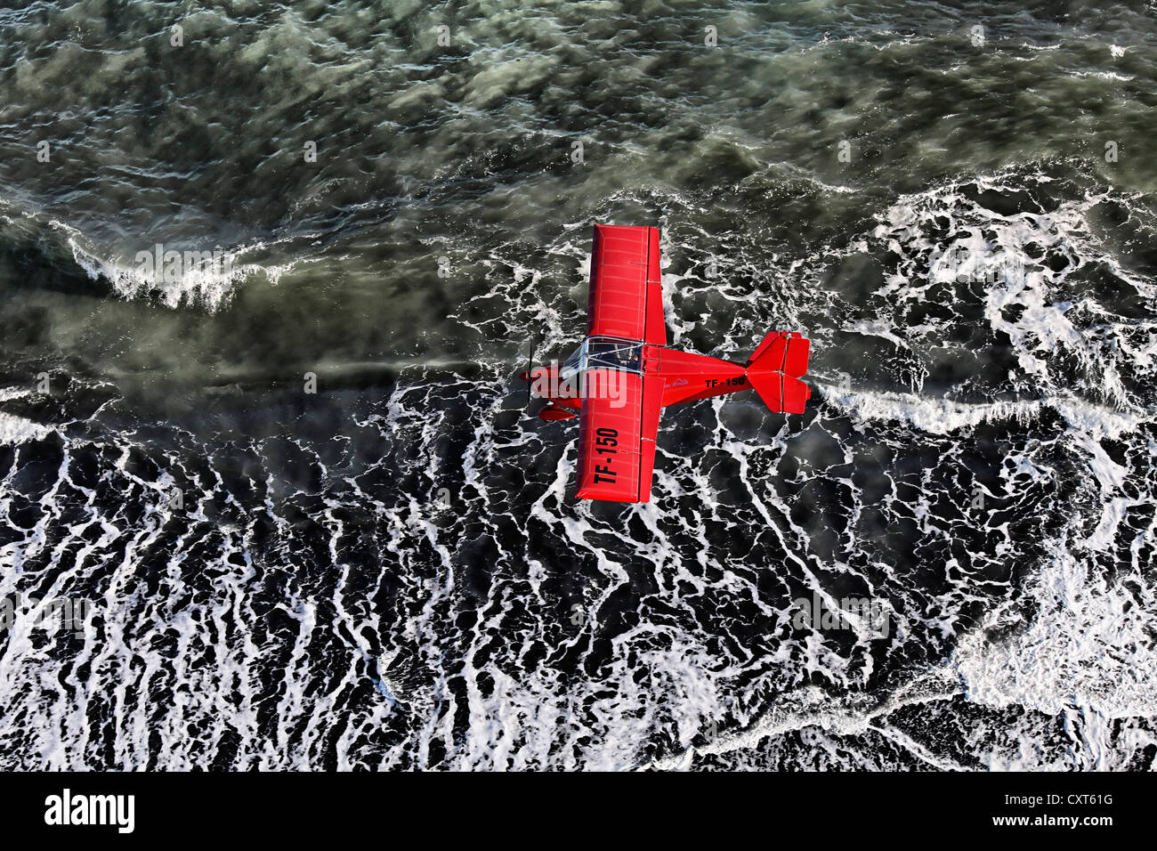 Aerial view, a red single-engine lightweight airplane flying over the waves of the North Atlantic, black lava coast, Iceland Stock Photo