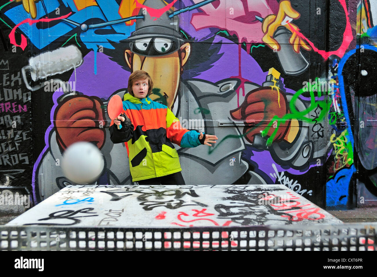 Twelveyearold boy playing table tennis in front of a graffiti wall, a