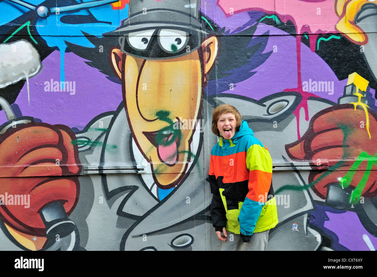 Boy, 12, cheekily poking out his tongue in front of a wall with graffiti, Cologne, North Rhine-Westphalia, PublicGround Stock Photo