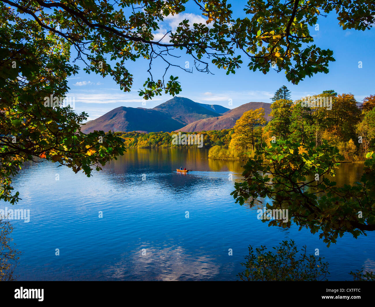 Two people out in a rowing boat on the still waters of Derwent Water in the Lake District National Park. Keswick, Cumbria, England. Stock Photo