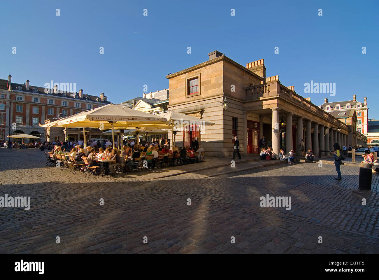 Horizontal wide angle of people enjoying a leisurely drink in the evening sun at one of the street cafes in Covent Garden. Stock Photo