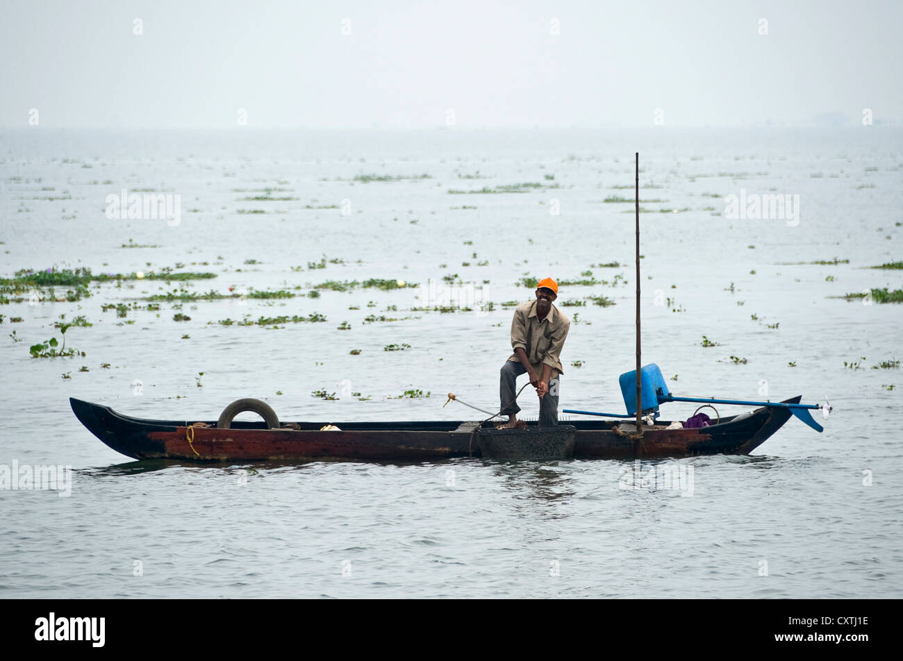Horizontal view of a traditional fisherman in his fishing boat out on the backwaters of Kerala, fishing for mussels. Stock Photo