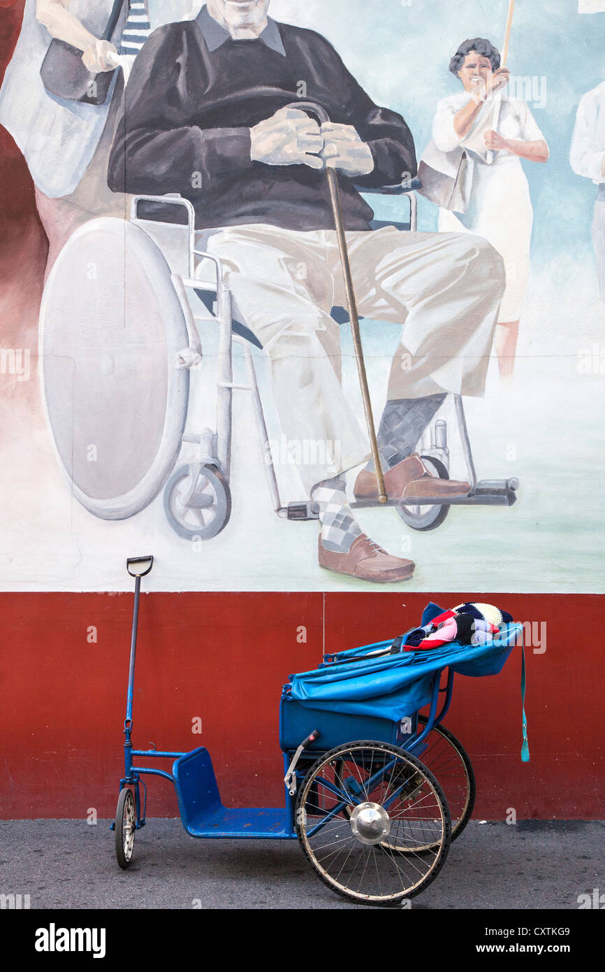 Wheel chair pulled by a Brancadier below a wallpainting of a disabled man, Lourdes, Hautes Pyrenees, France Stock Photo