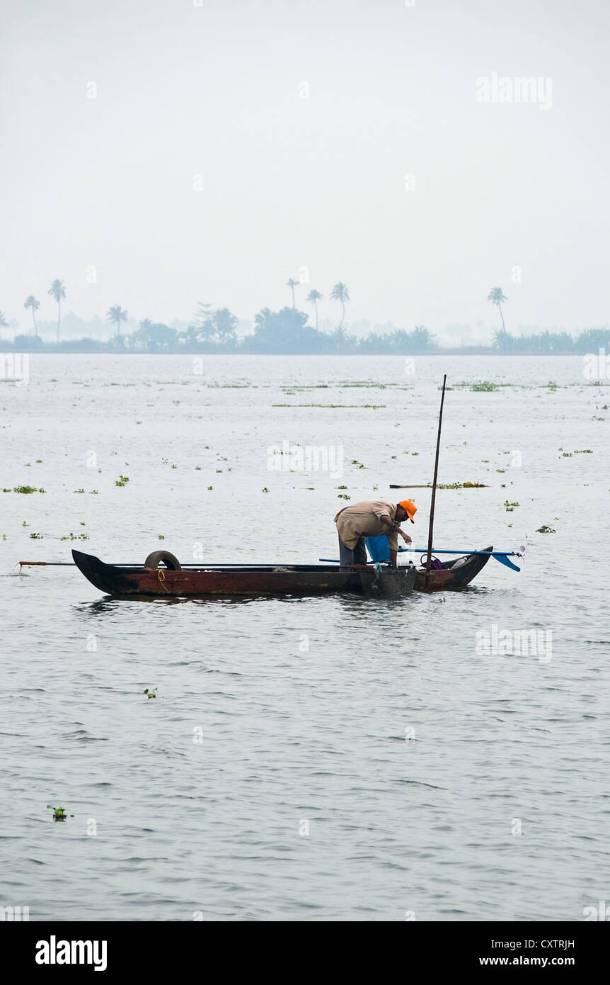 Vertical view of a traditional fisherman in his fishing boat out on the backwaters of Kerala, fishing for mussels. Stock Photo