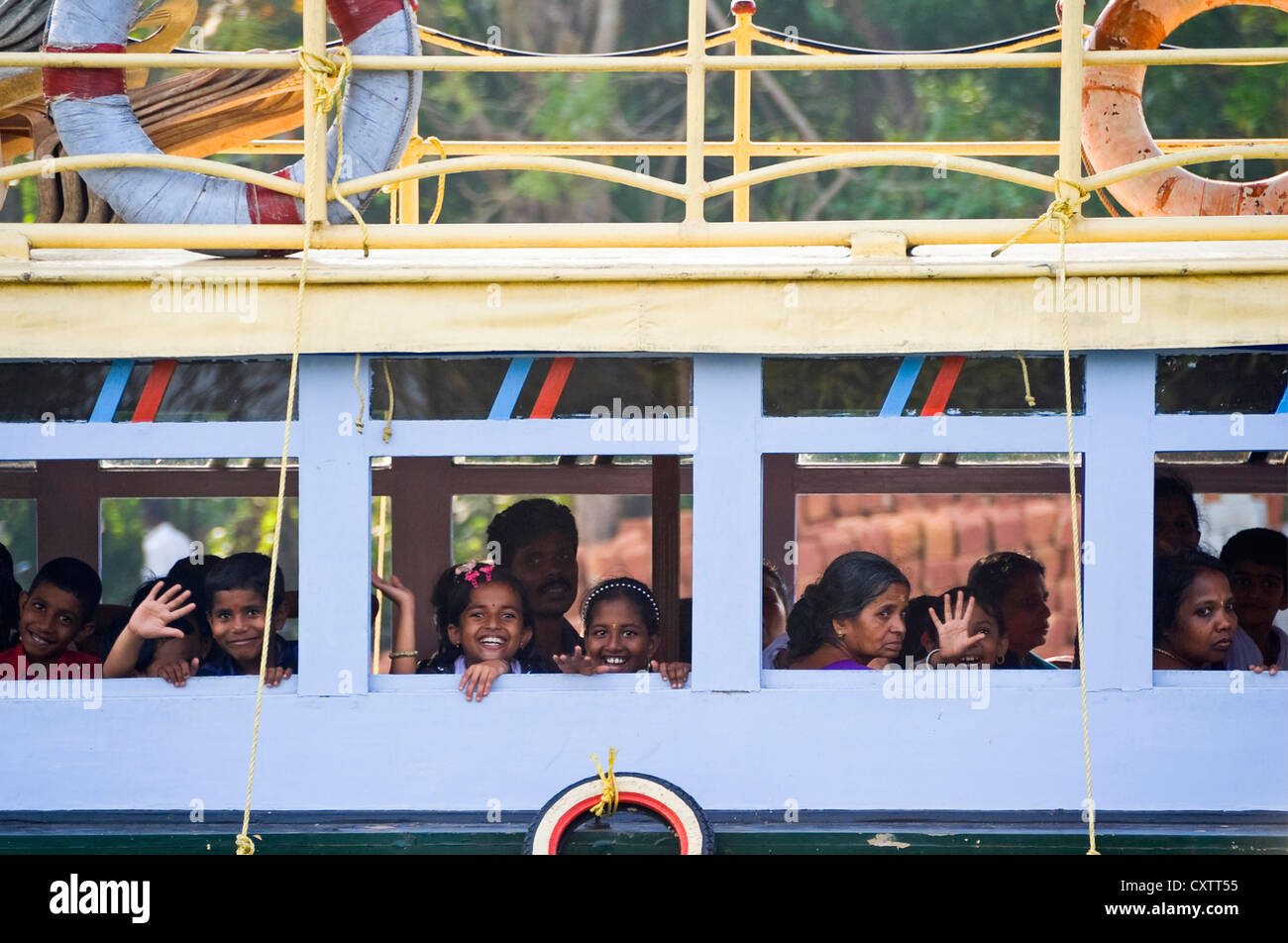 Horizontal view of school children waving and smiling from a public ferry in the backwaters of Kerala. Stock Photo