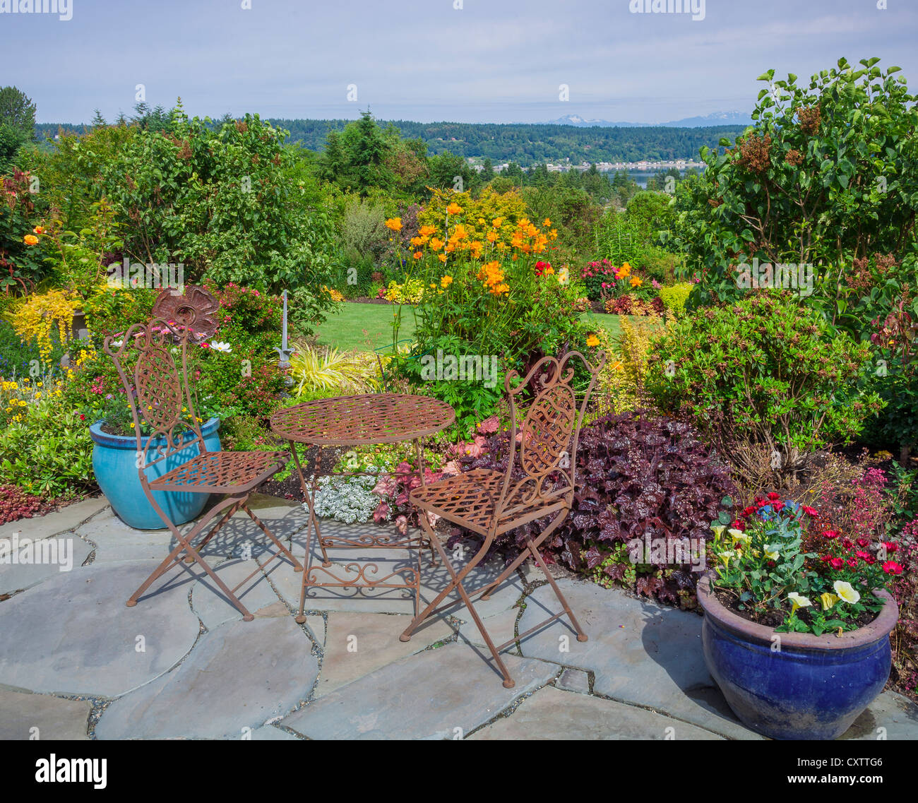 Vashon-Maury Island, WA: Iron table and chairs on flagstone patio with a view of a terraced garden and of Quartermaster Harbor Stock Photo