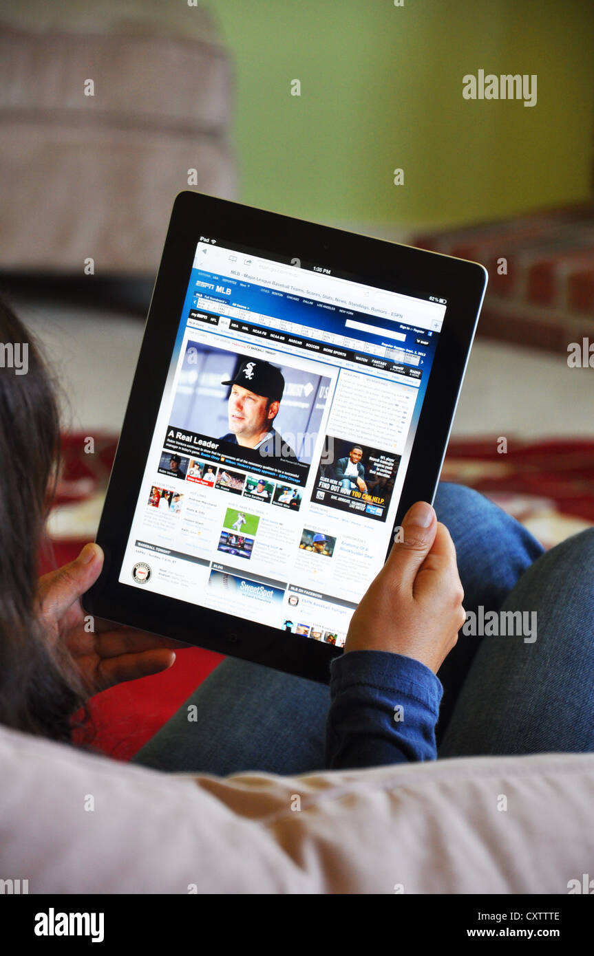 Young girl with iPad sitting on sofa at home. Major League Baseball (MLB) website shown on the iPad screen. Stock Photo