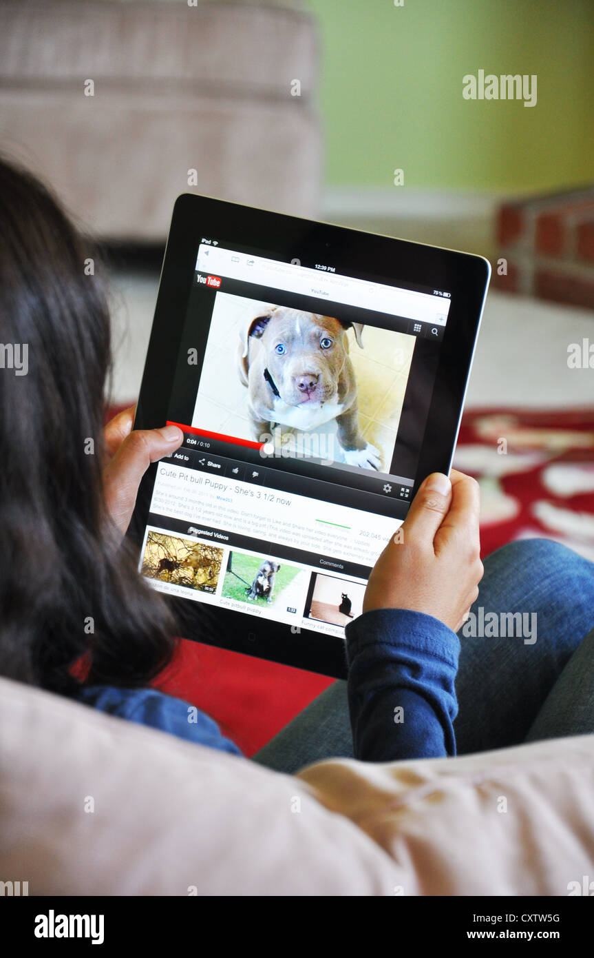 Young girl with iPad sitting on sofa at home. Youtube funny video website shown on the iPad screen. Stock Photo