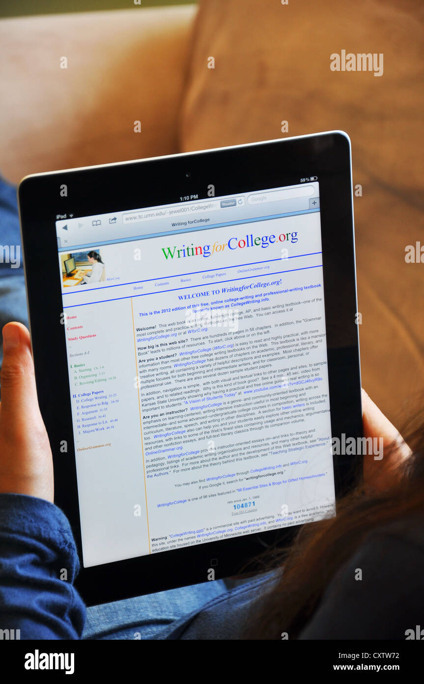 Female student with iPad sitting on sofa at home. Writing for College website shown on the iPad screen. Stock Photo