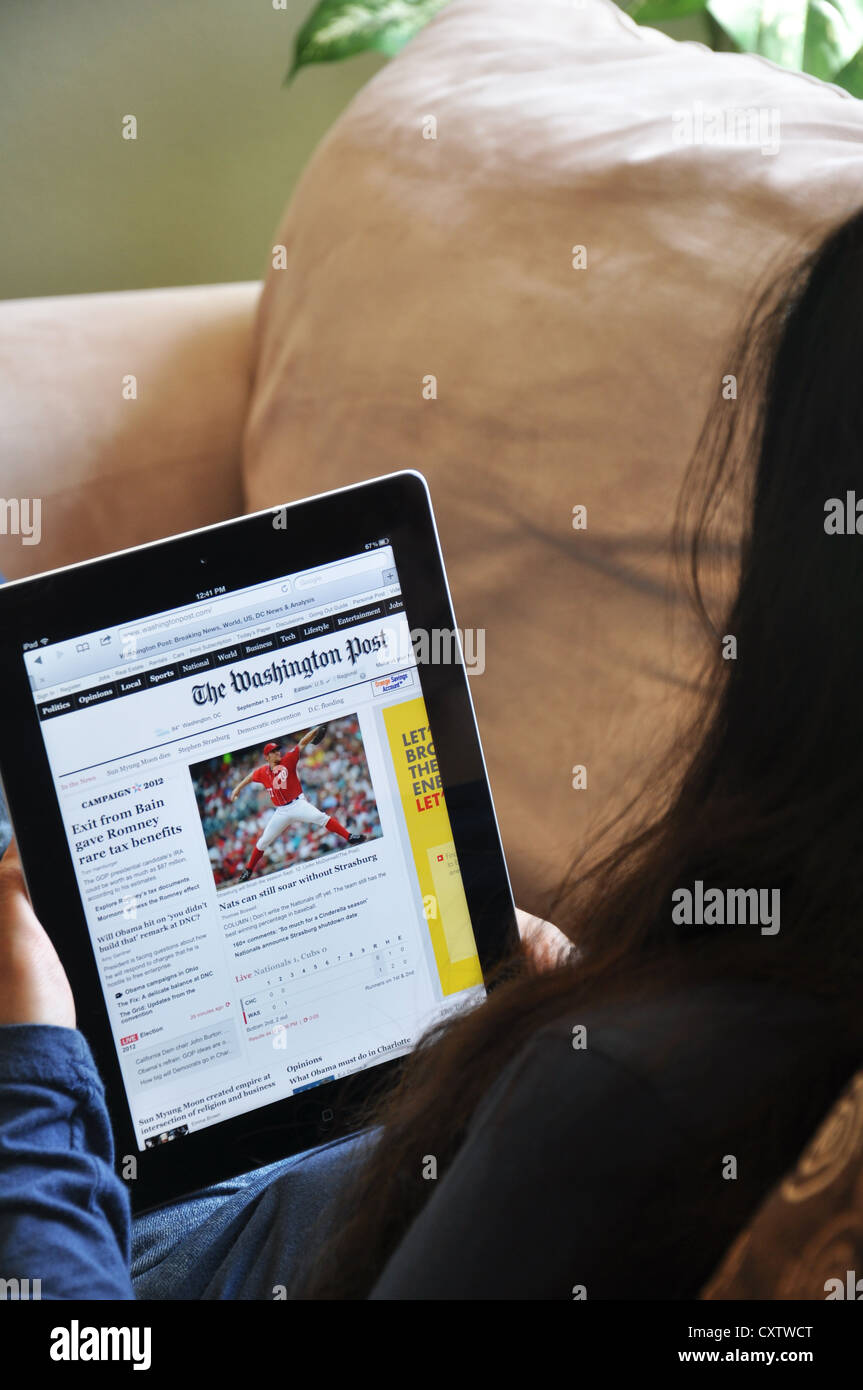 Young woman with iPad sitting on sofa at home.  Washington Post website shown on the iPad screen. Stock Photo