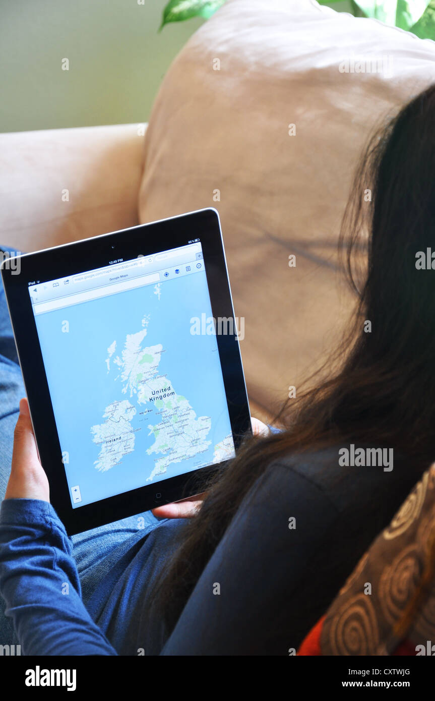 Young woman with iPad sitting on sofa at home. UK map shown on the iPad screen. Stock Photo