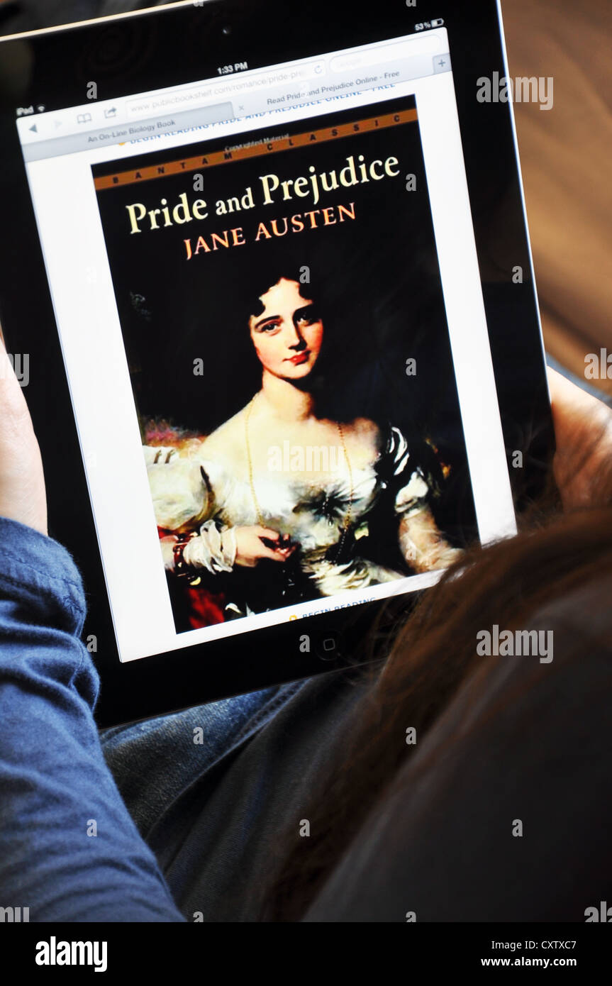 Young girl with iPad sitting on sofa at home. Pride and Prejudice book by Jane Austen shown on the iPad screen. Stock Photo