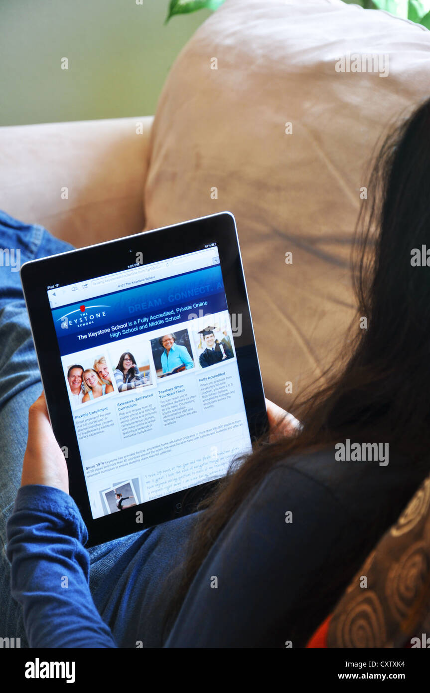 Young girl with iPad sitting on sofa at home. Online school website shown on the iPad screen. Stock Photo