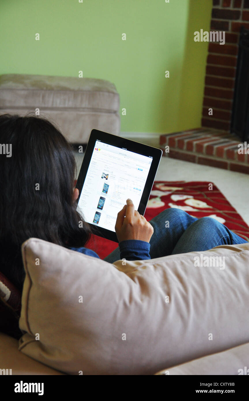 Young girl with iPad sitting on sofa at home shopping online for iPod. Stock Photo
