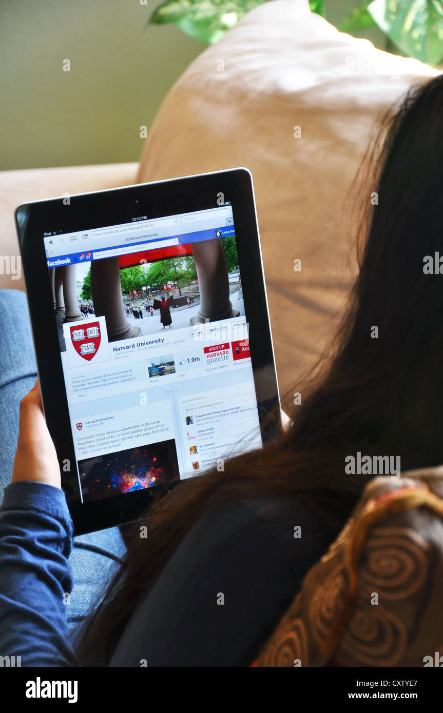 Female student with iPad sitting on sofa at home. Harvard University website shown on the iPad screen. Stock Photo