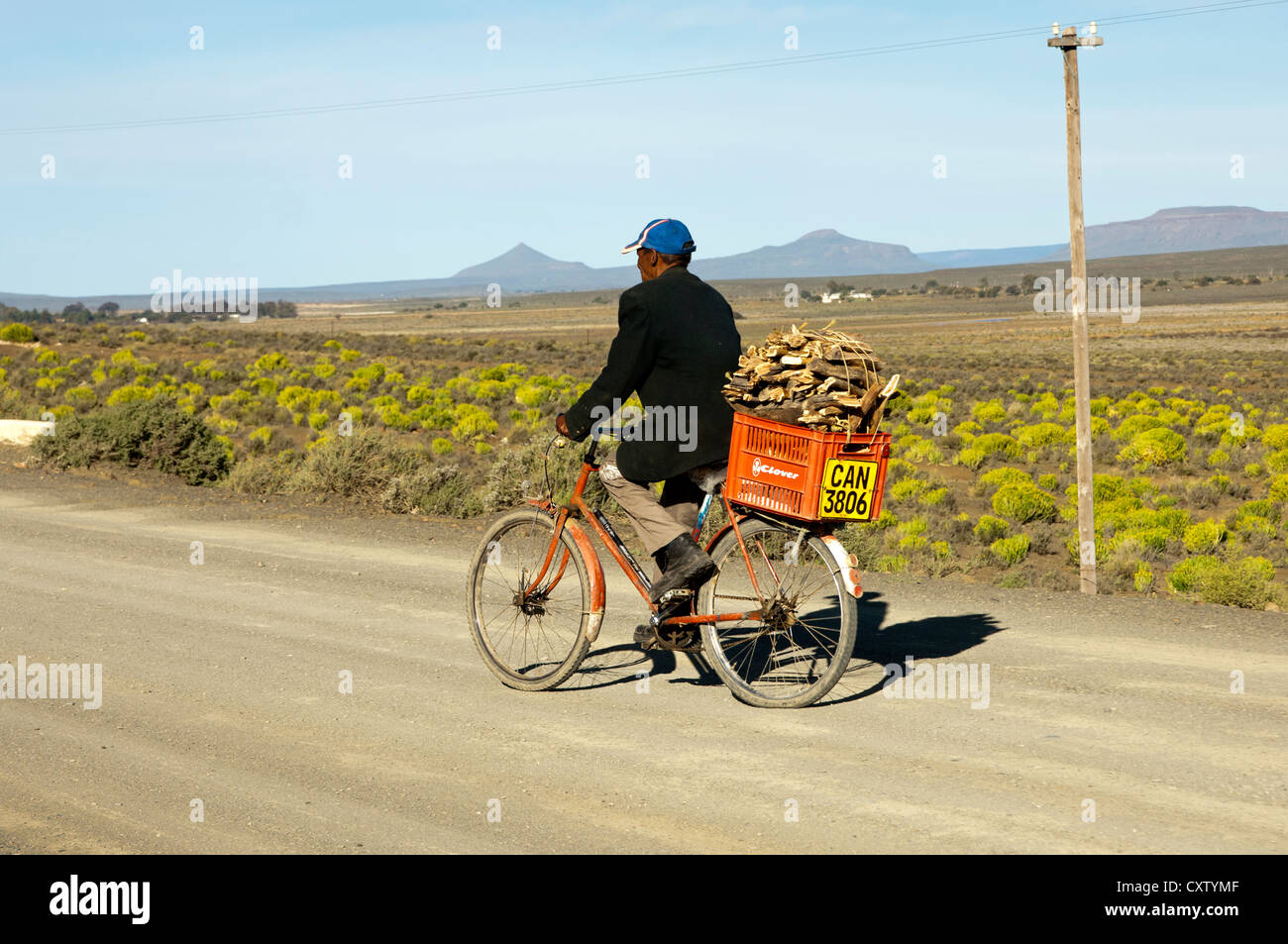 Local man biking on a country road to Calvinia with a box of firewood on the luggage carrier, Calvinia, South Africa Stock Photo