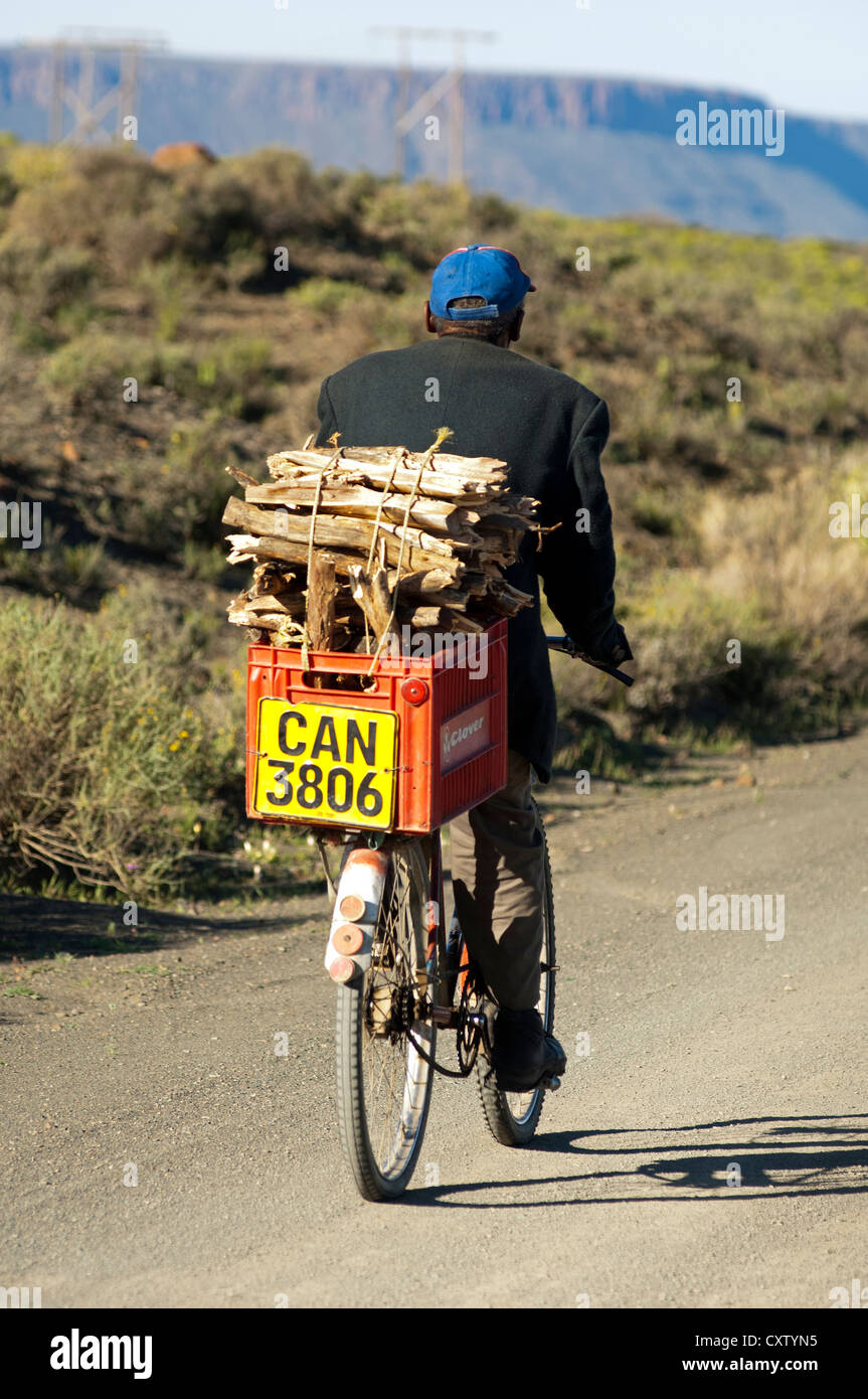 man biking on a country road to Calvinia with a box of firewood on the luggage carrier, Calvinia, South Africa Stock Photo