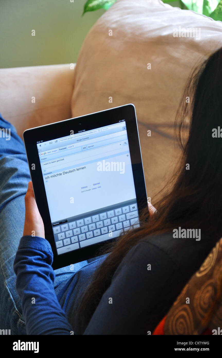 Female student with iPad sitting on sofa at home. German translator website shown on the iPad screen. Stock Photo