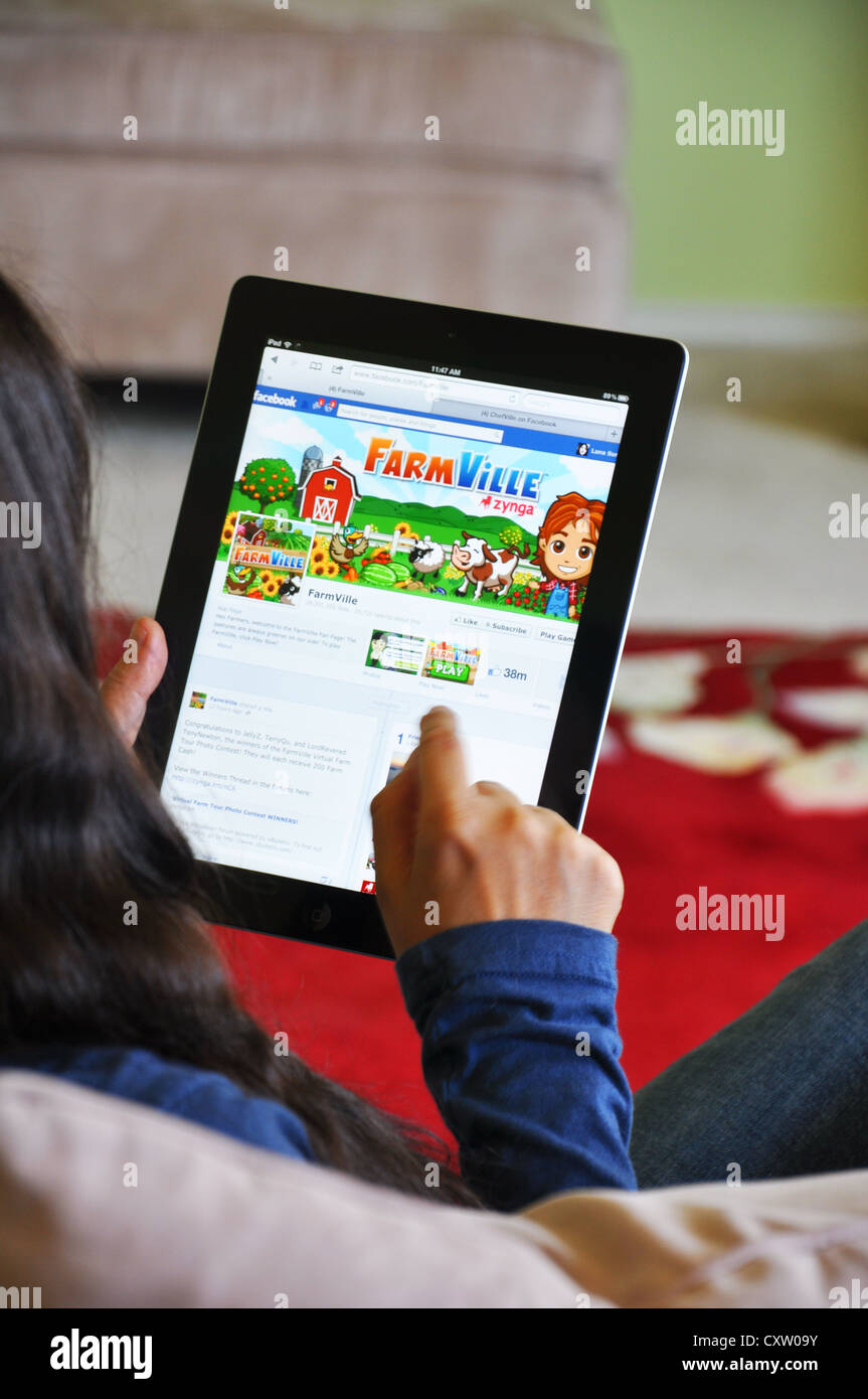 Young girl with iPad sitting on sofa at home. Facebook Farmville game shown on the iPad screen. Stock Photo