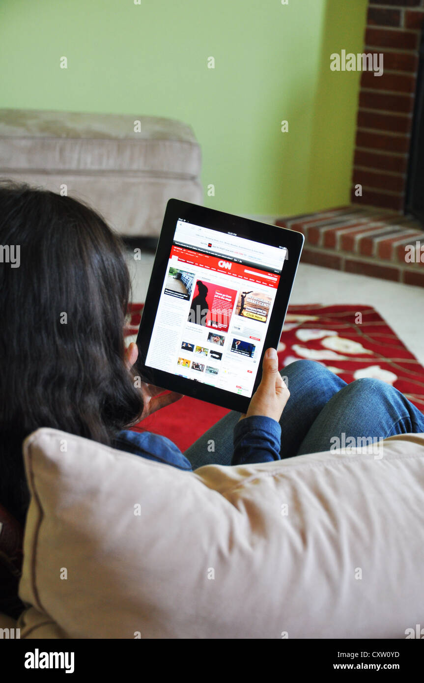 Young girl with iPad sitting on sofa at home. CNN news website shown on the iPad screen. Stock Photo