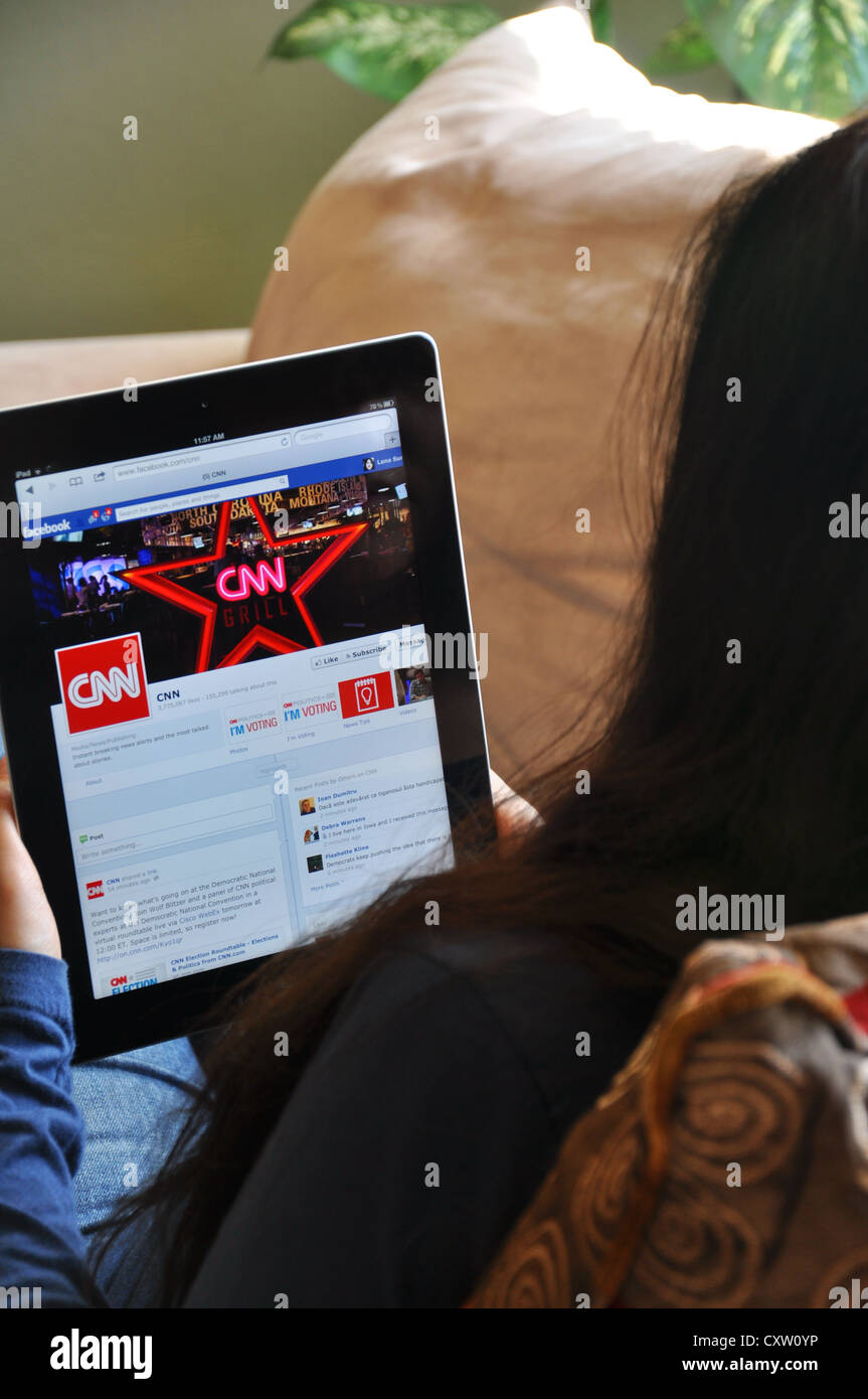 Young girl with iPad sitting on sofa at home. Facebook CNN news website shown on the iPad screen. Stock Photo