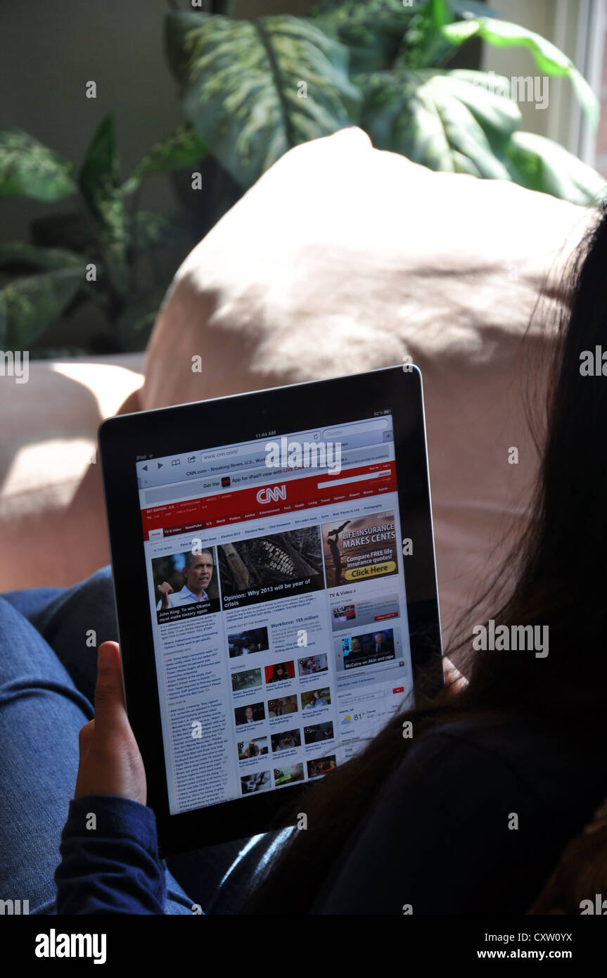 Young girl with iPad sitting on sofa at home. CNN news website shown on the iPad screen. Stock Photo