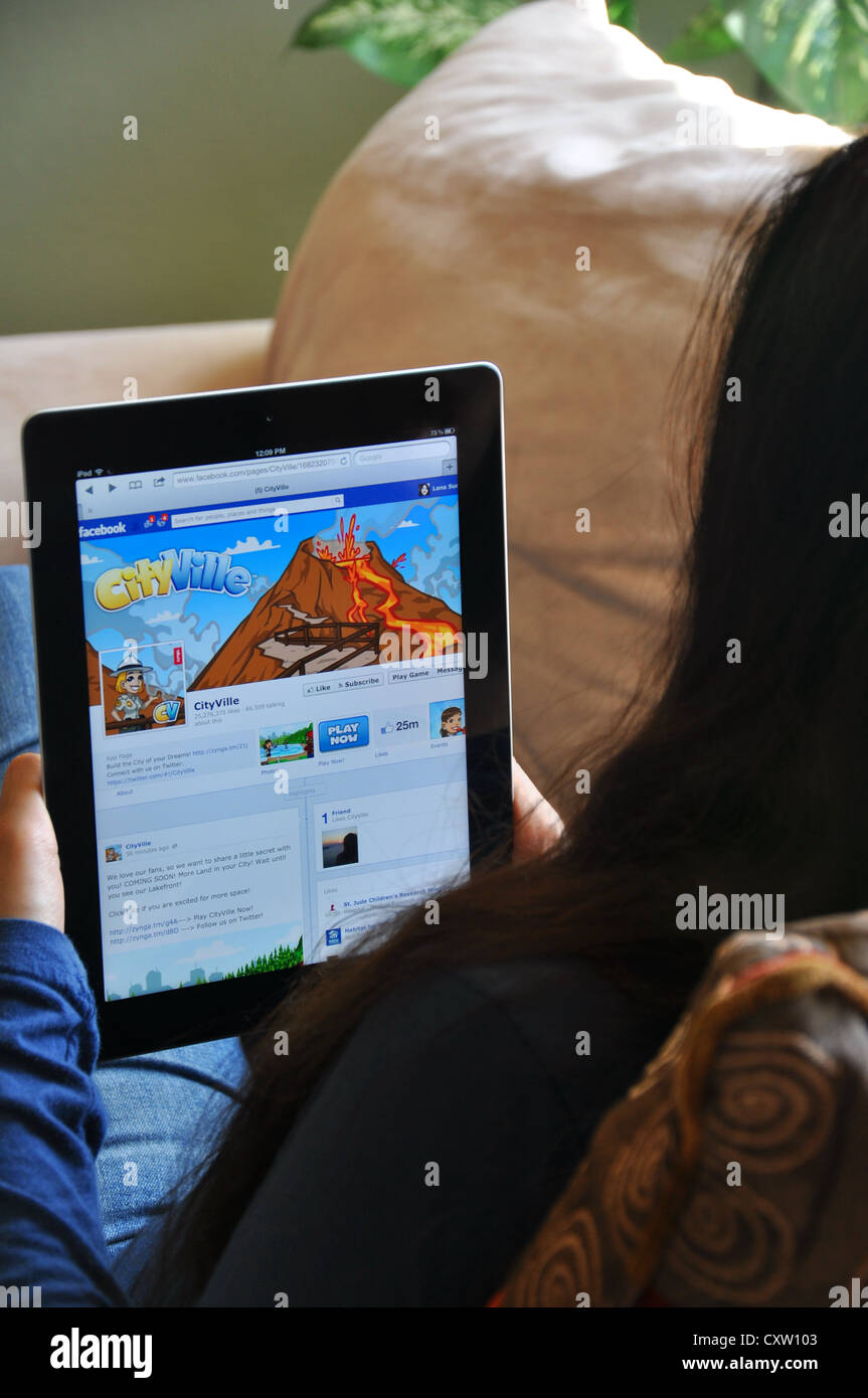 Young girl with iPad sitting on sofa at home. Facebook Cityville game shown on the iPad screen. Stock Photo