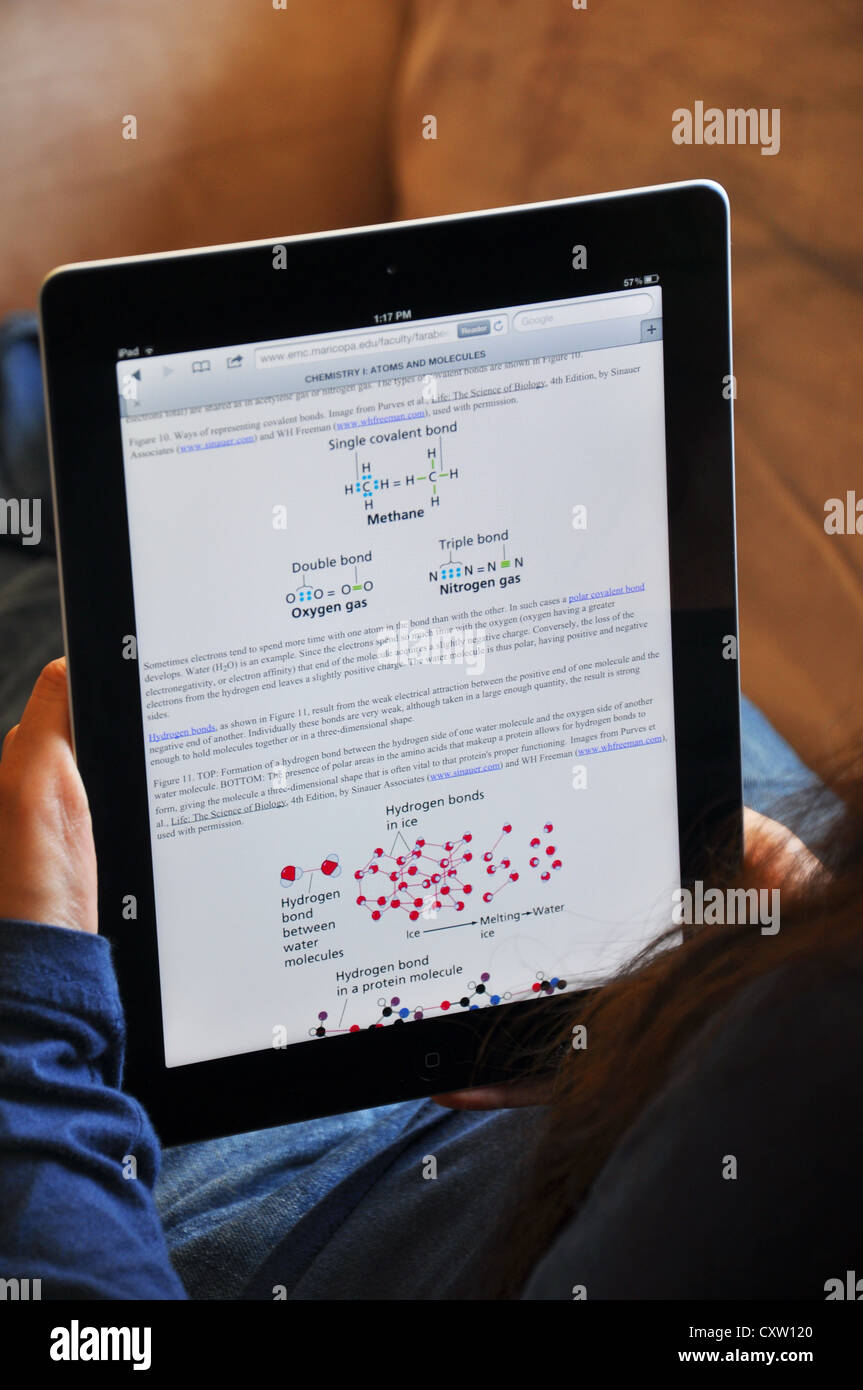 Female student  with iPad sitting on sofa at home. Chemistry textbook shown on the iPad screen. Stock Photo