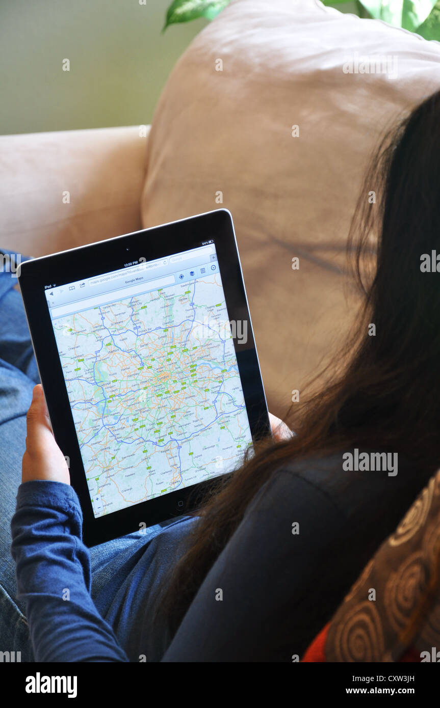 Young girl with iPad sitting on sofa at home. London map website shown on the iPad screen. Stock Photo