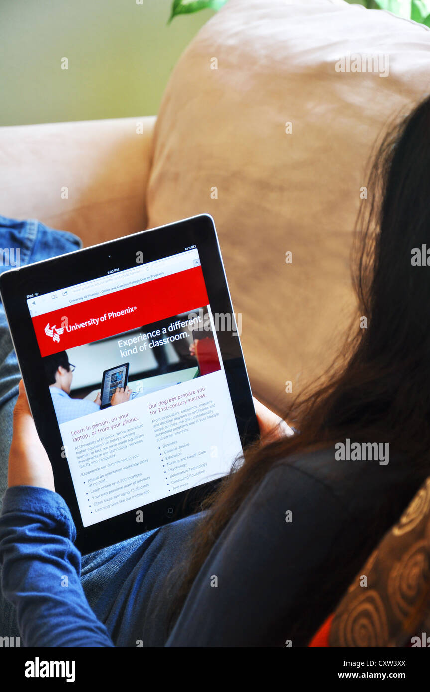 Young girl with iPad sitting on sofa at home. University of Phoenix website shown on the iPad screen. Stock Photo