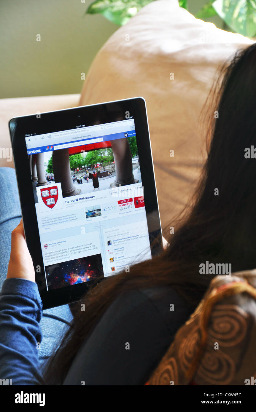 Student with iPad looking at Harvard University website, sitting on sofa at home Stock Photo