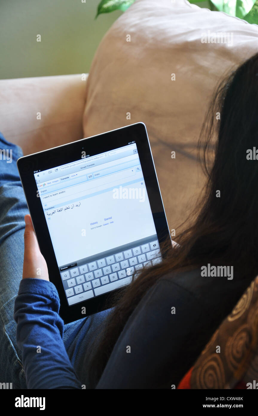 Female student with iPad sitting on sofa at home. Arabic translator website shown on the iPad screen. Stock Photo