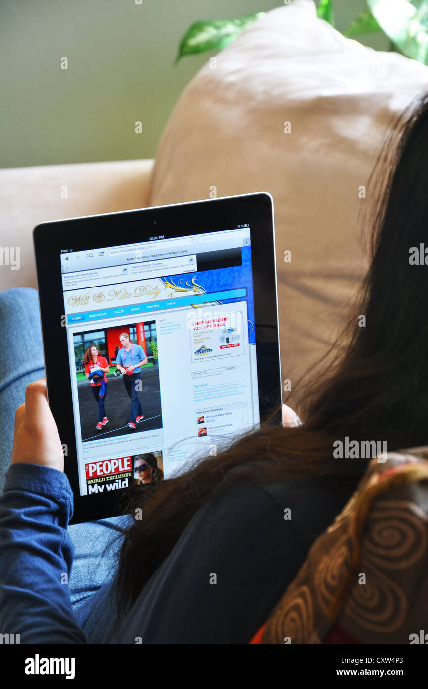 Young girl with iPad sitting on sofa at home. Kate & Will Daily website shown on the iPad screen. Stock Photo
