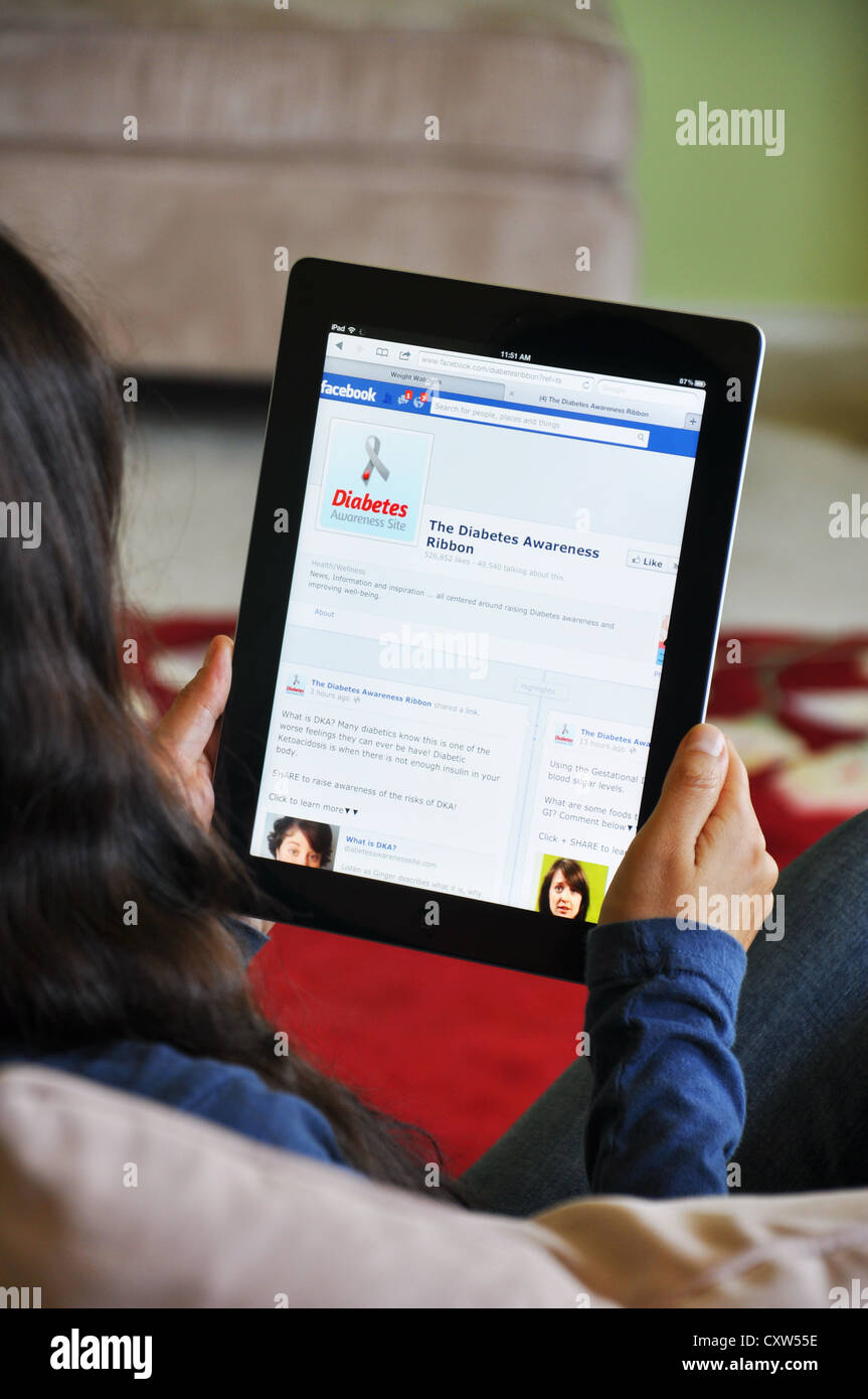 Young girl with iPad sitting on sofa at home. Facebook Diabetes website shown on the iPad screen. Stock Photo