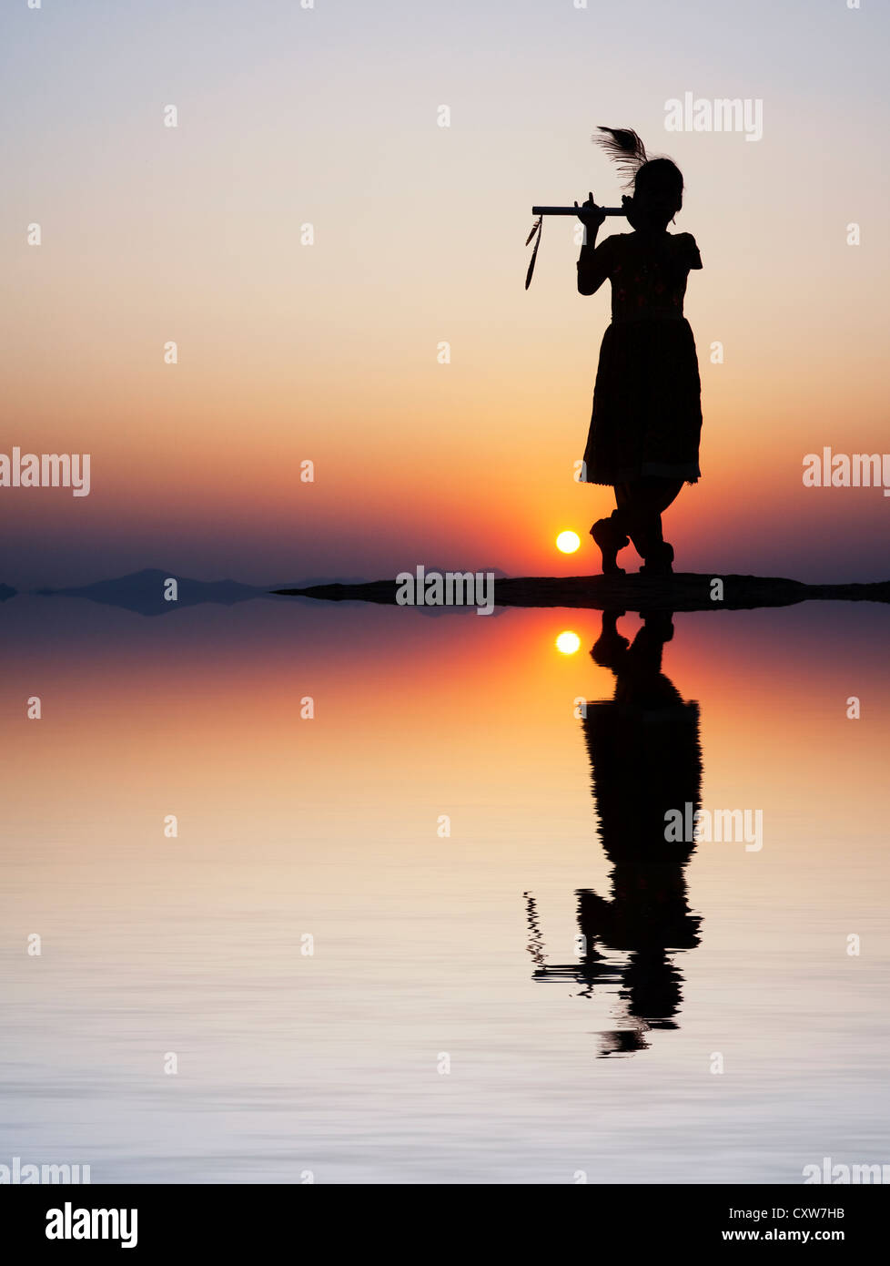 Silhouette of an Indian girl pretending to be Lord krishna at sunset with water reflection and ripples. India Stock Photo