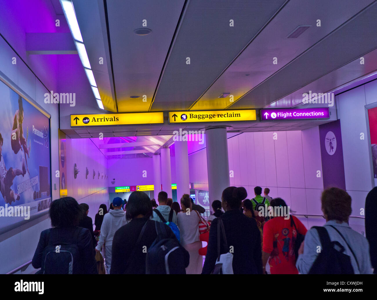 ARRIVALS Airline passengers arriving at Heathrow airport walkway lit by calming suffused colours heading for arrivals and baggage reclaim areas Stock Photo