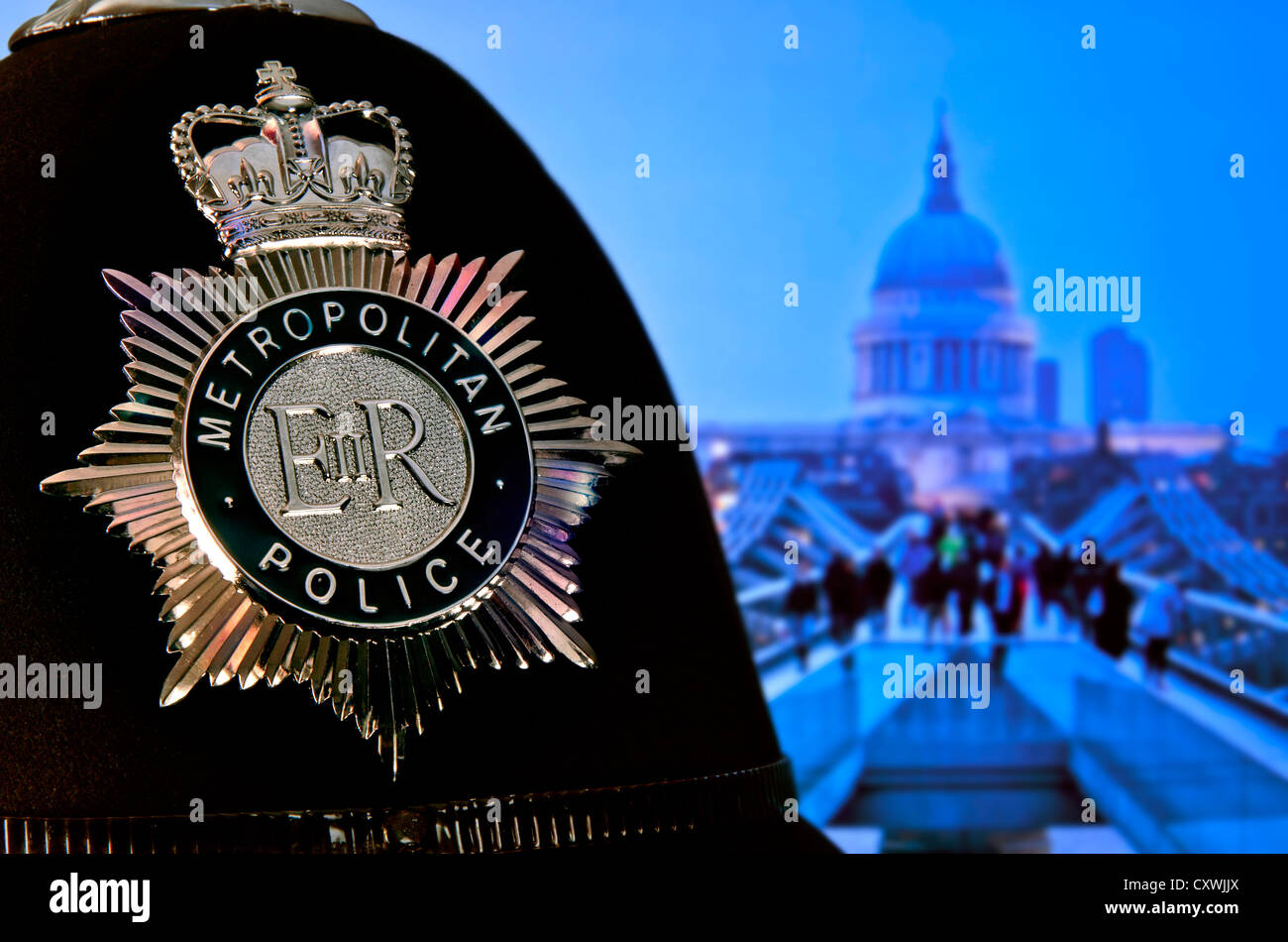Metropolitan police constable helmet and badge with Saint Paul's Cathedral and Millennium Bridge London at dusk UK Stock Photo