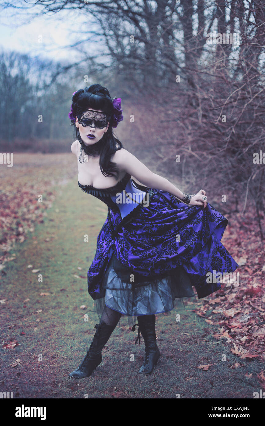 gothic young woman in the woods curtsies, wearing a fancy purple gown and a  mysterious blindfold over her eyes Stock Photo - Alamy