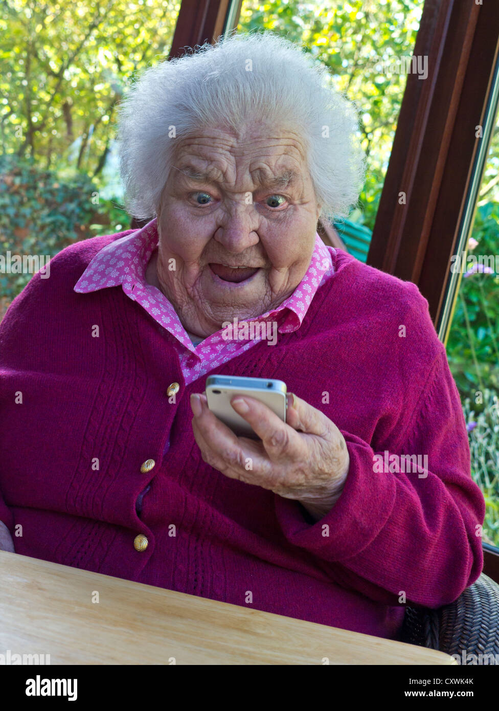Elderly technology vulnerable senior old lady isolating at home amazed by new family friends safe communication on her iPhone smartphone mobile phone Stock Photo