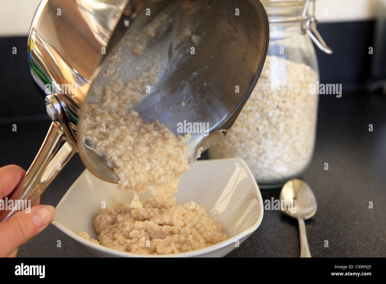 Pouring breakfast porridge from a cooking pot into a bowl Stock Photo