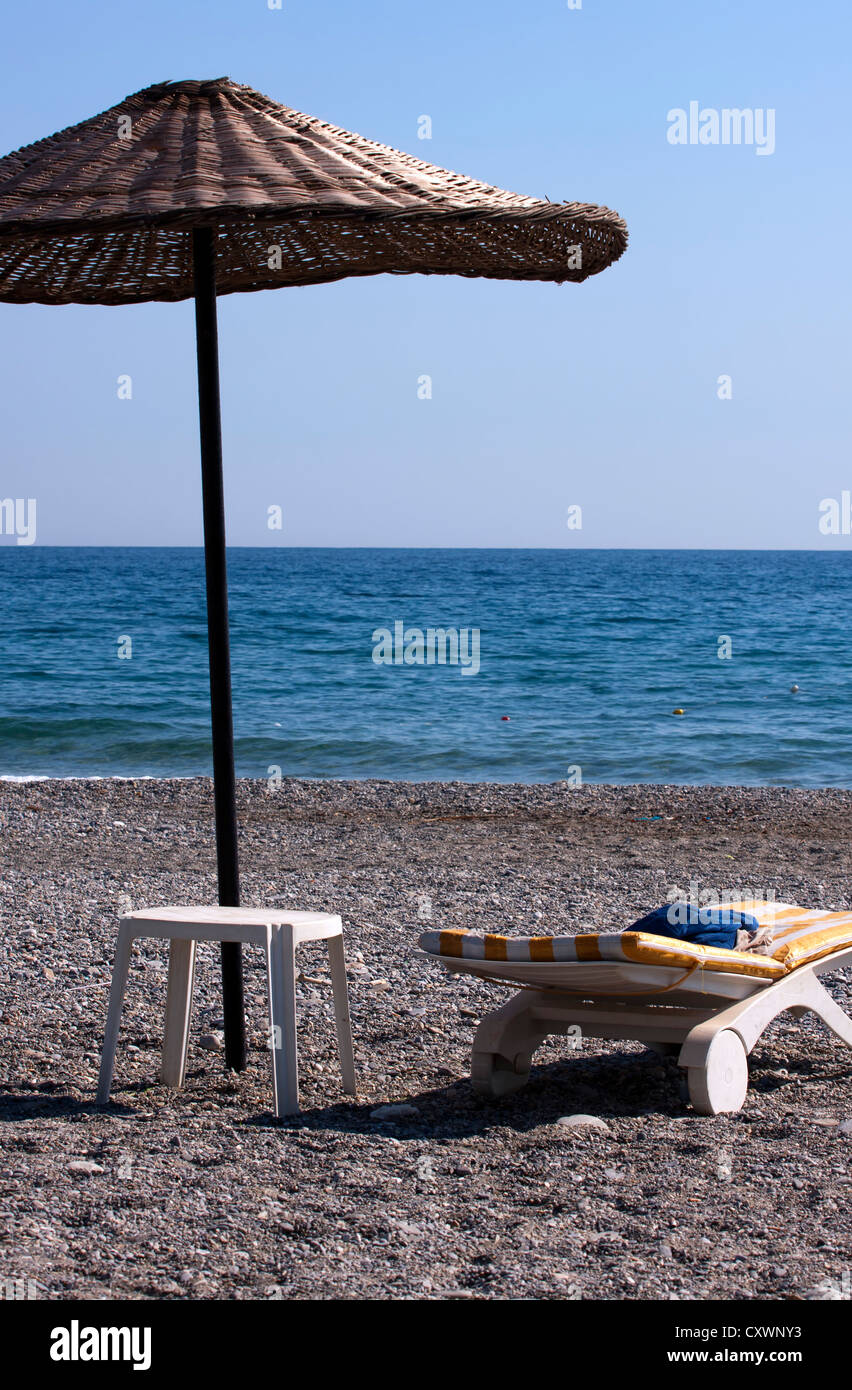 Plastic sun lounger with simple table and a beach umbrella on a deserted beach. Stock Photo