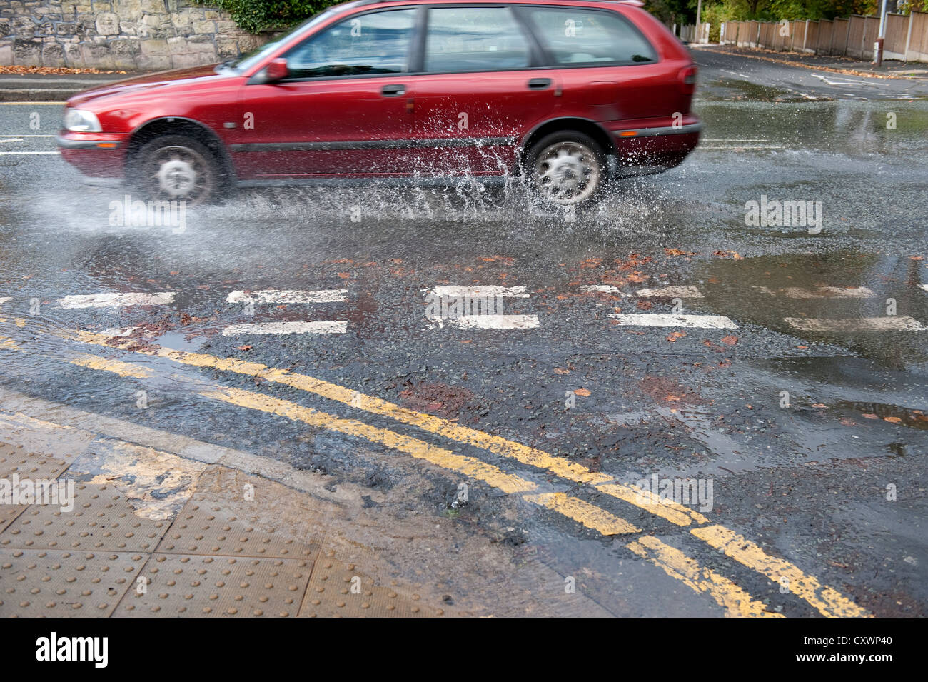 Burst water main pipe flooding road with cars going past Stock Photo