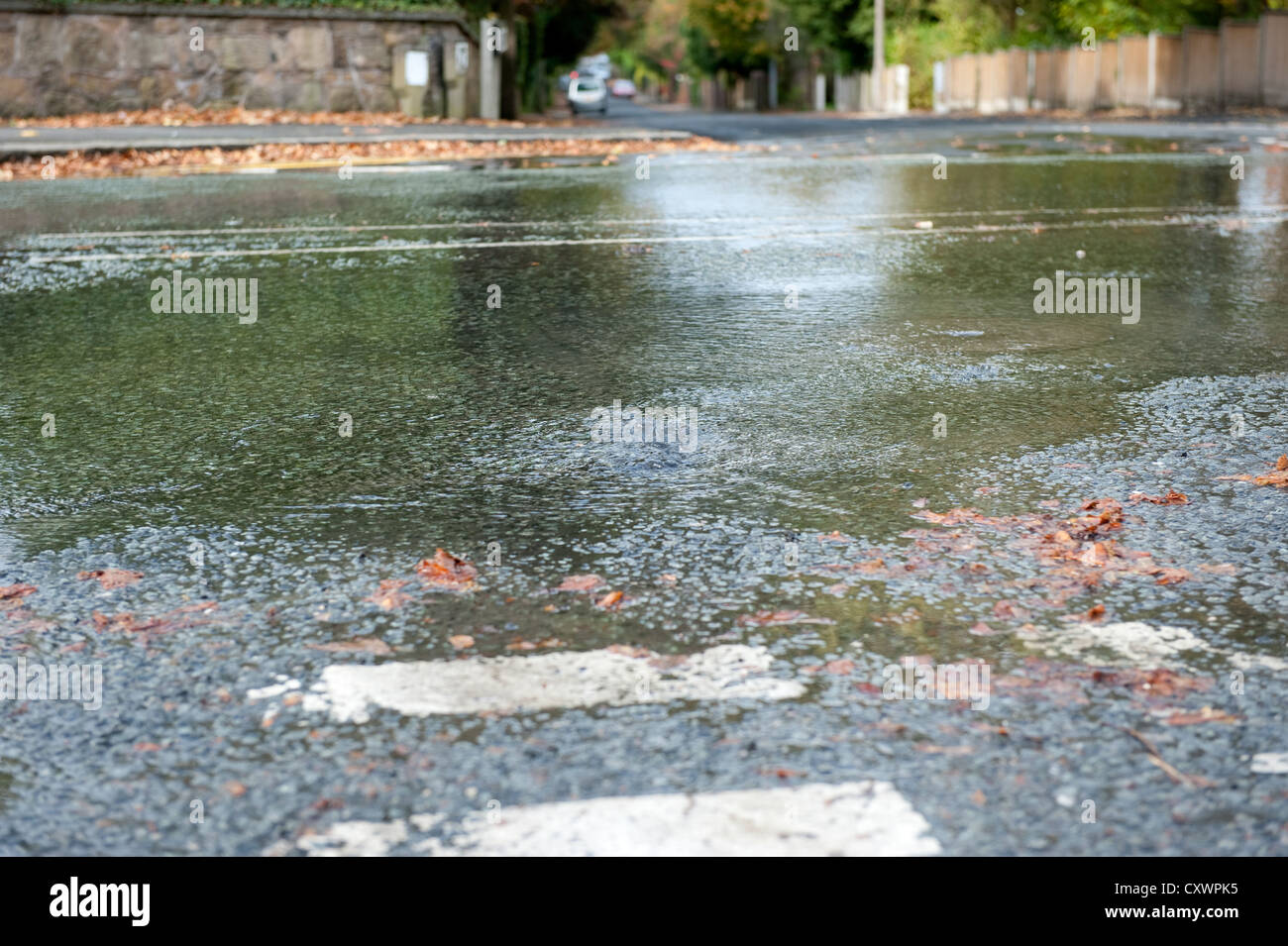 Burst water main pipe flooding road with cars going past Stock Photo