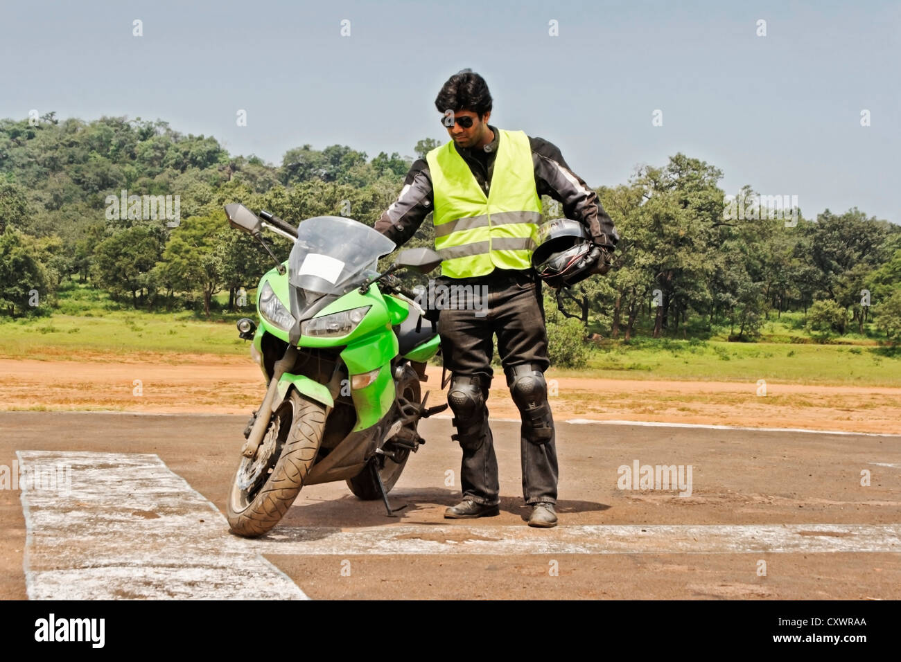 Motorbiker stood by the side of his bike inserting ignition key, looks