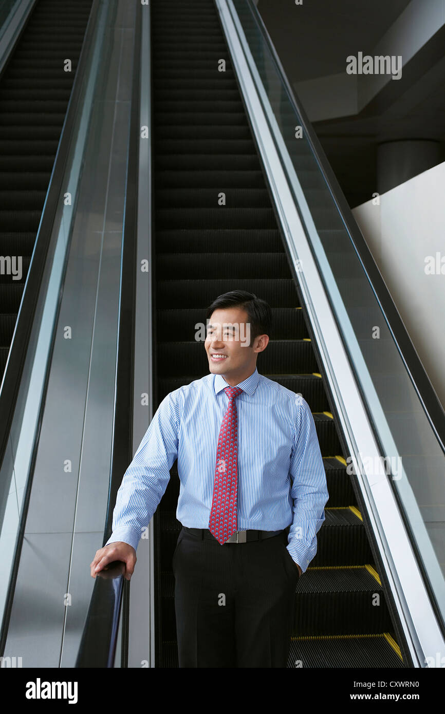Businessman riding escalator in office Stock Photo